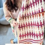 A person holds a colorful, patterned mosaic crochet blanket in a cozy living room setting. The text reads "Inset Mosaic Crochet Blanket Pattern & Video, No Tails technique.