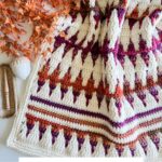 Colorful crochet blanket with geometric patterns, bordered by autumn leaves and a white decorative shell, accompanied by crafting tools. Text reads "Inset Mosaic Crochet Blanket Pattern & Video." Discover the art of mosaic crochet with this vibrant design.