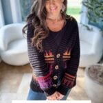 A woman wearing a black cardigan with colorful patterns stands indoors. A text overlay reads, "Top-Down, Seamless Mosaic Crochet Cardigan Pattern XS-5X plus Video Tutorial.