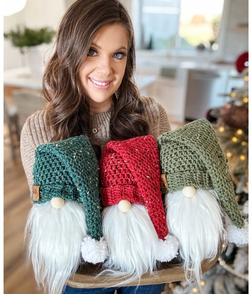 A person holding three delightful crochet gnome decorations, each adorned with a charming green, red, or green hat and soft white beards.