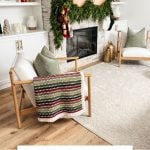 Cozy living room with a fireplace adorned with a garland and stockings, two chairs, and a crocheted blanket on one chair. Text reads: "Holiday Weave Moss Stitch Blanket Crochet Pattern & Video.