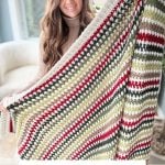 Person proudly holding a crochet blanket featuring a vibrant striped moss stitch pattern in green, red, and white hues. Text reads: "Moss Stitch Blanket - Crochet Pattern & Video.