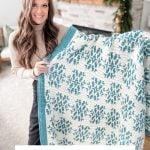 A woman holds up a white and teal snowflake blanket in a living room with a stone fireplace and greenery on the mantel. Text reads: "Snow Flurries Mosaic Blanket Overlay Crochet Pattern & Video.