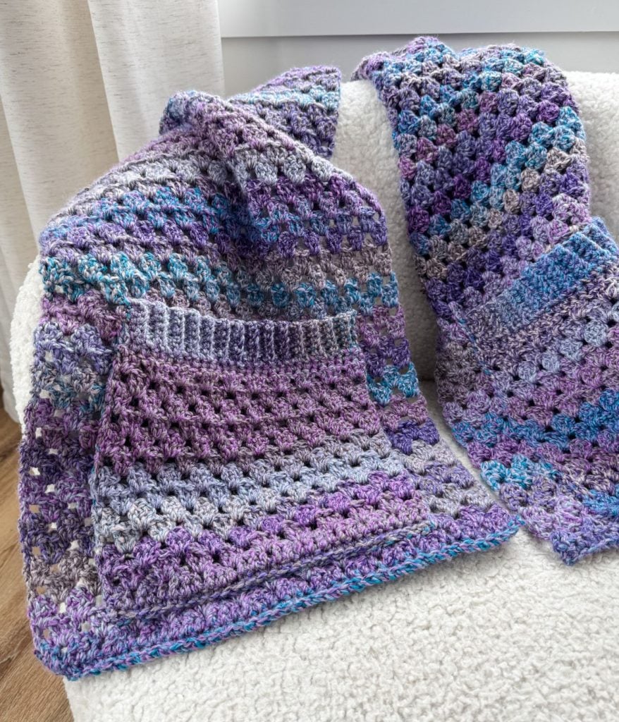 A cozy scene with purple and blue crocheted blankets draped over a white armchair, accompanied by a stylish pocket shawl for added warmth.