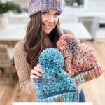 A person smiles while holding three colorful crochet hats with pom-poms. Text reads: "Chunky Granny Stitch Hat - Free Crochet Pattern + Video.