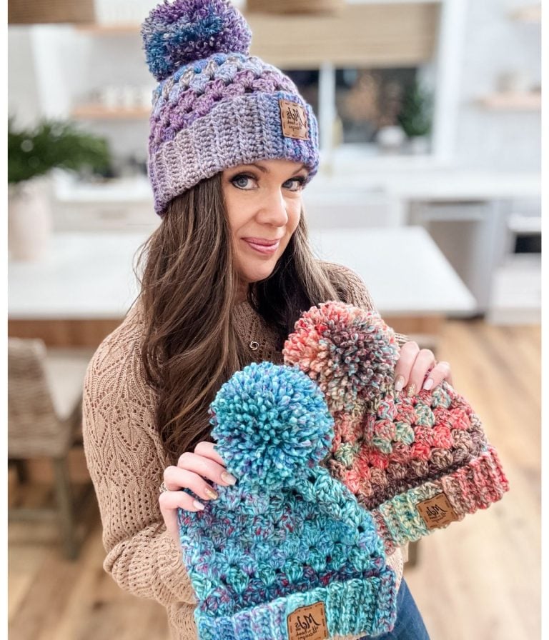 In a cozy kitchen, someone proudly displays three vibrant crochet hats adorned with playful pom-poms on top, each made using the chunky granny stitch technique.