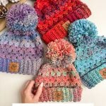 Four colorful crocheted hats with pom-poms are displayed on a surface, showcasing the Chunky Granny Stitch design. A hand is holding the bottom left hat. Decorative pine cones and a promotional text for this unique crochet pattern are also visible.