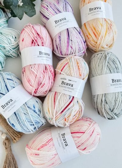 Assorted skeins of Brava worsted weight yarn in various colors arranged on a white surface, perfect for crafting your first Snowy Season Beanie with our free pattern.