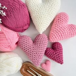 Crochet heart shapes in shades of pink and white are arranged with matching yarn balls and crochet hooks on a light surface, creating a harmonious display.