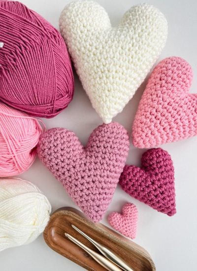 Crochet heart shapes in shades of pink and white are arranged with matching yarn balls and crochet hooks on a light surface, creating a harmonious display.