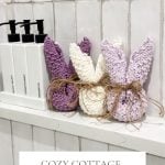 Three crochet dishcloths in pastel colors, tied with twine, are displayed on a bathroom shelf next to white bottles labeled body wash, conditioner, and shampoo.