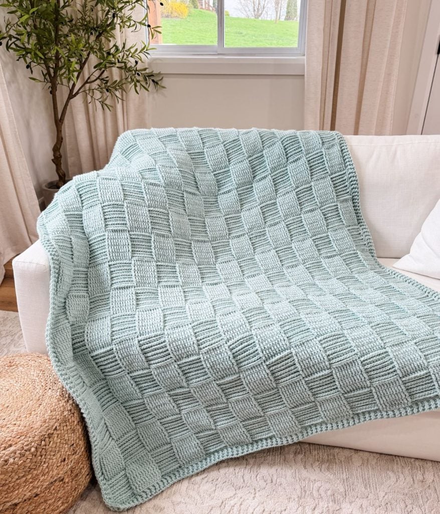 A light blue Basket Weave Blanket, featuring a classic basketweave pattern, is draped over a white sofa in a bright living room.