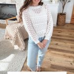 A woman stands indoors wearing the Caribbean Sea Sweater, a white crochet design paired with light blue jeans. Text below reads "Caribbean Sea Sweater - Crochet Pattern & Video.