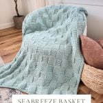 A light blue Basket Weave Blanket with a crochet pattern draped over a white chair, next to a potted plant and decorative pillows in a cozy room. Text reads: "Seabreeze Basket Weave Blanket.