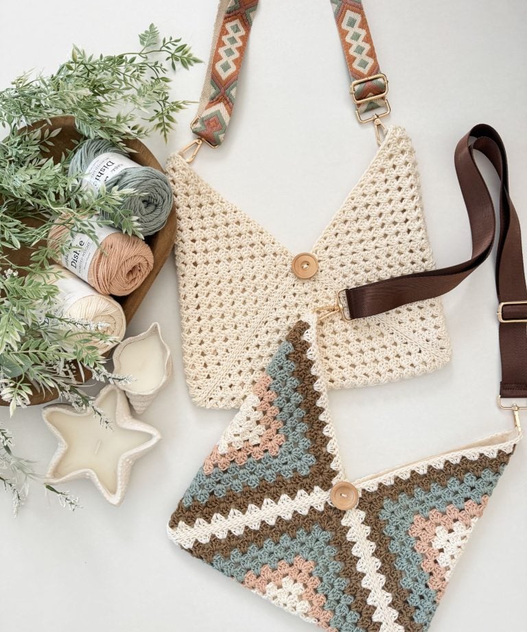 Two crochet crossbody bags with button closures lie on a surface, next to skeins of yarn, greenery, and two star-shaped candles—perfect as stylish beach bags for your summer outings.