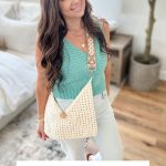 Woman wearing a teal crochet top and holding a cream-colored Caribbean beach bag with a button closure, standing indoors on a rug beside a plant. Text reads: “Caribbean Beach Bag Easy Crochet Pattern & Video.”.