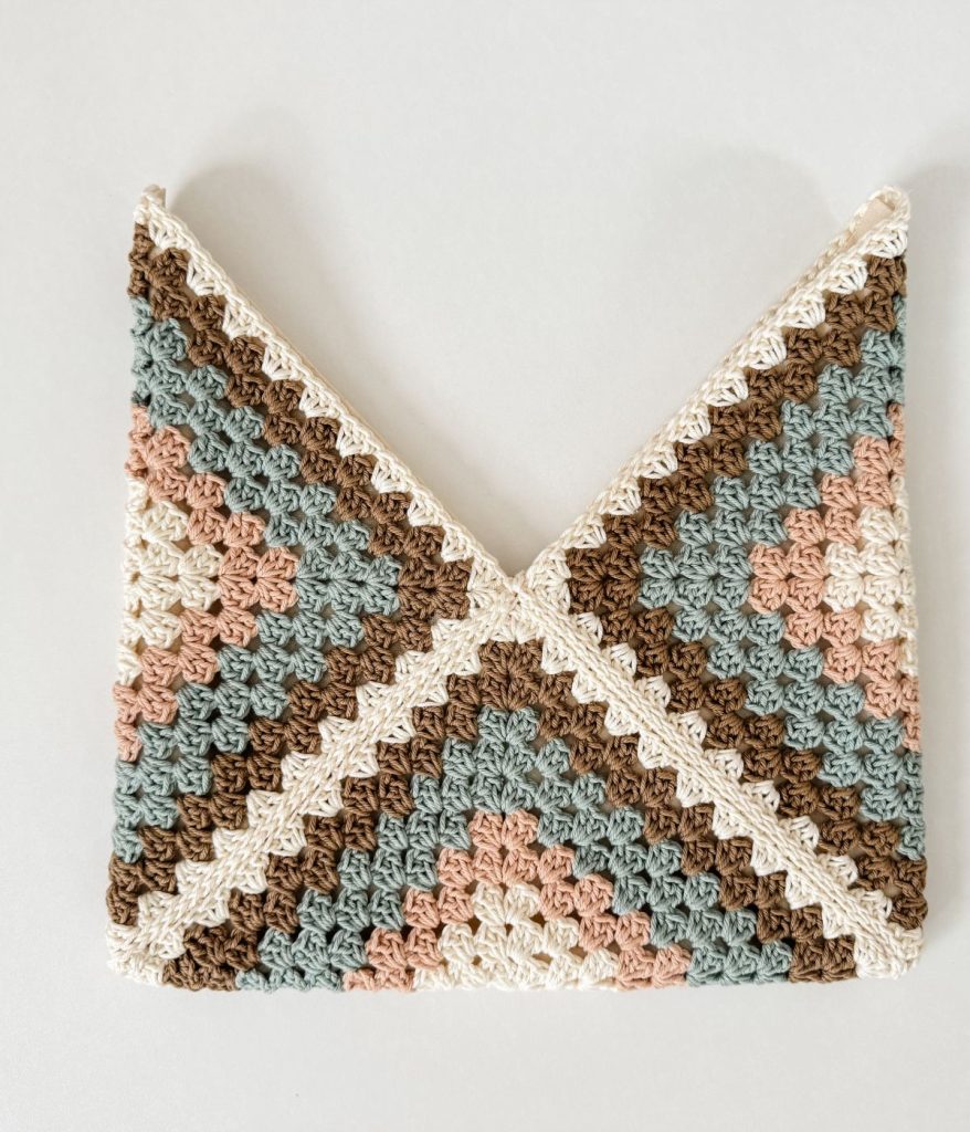 A crocheted envelope-style pouch with a geometric crochet pattern in cream, brown, pink, and green yarn.