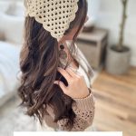 Woman wearing a beige crochet bandana with a granny square pattern, standing indoors with long hair and a neutral-toned outfit.