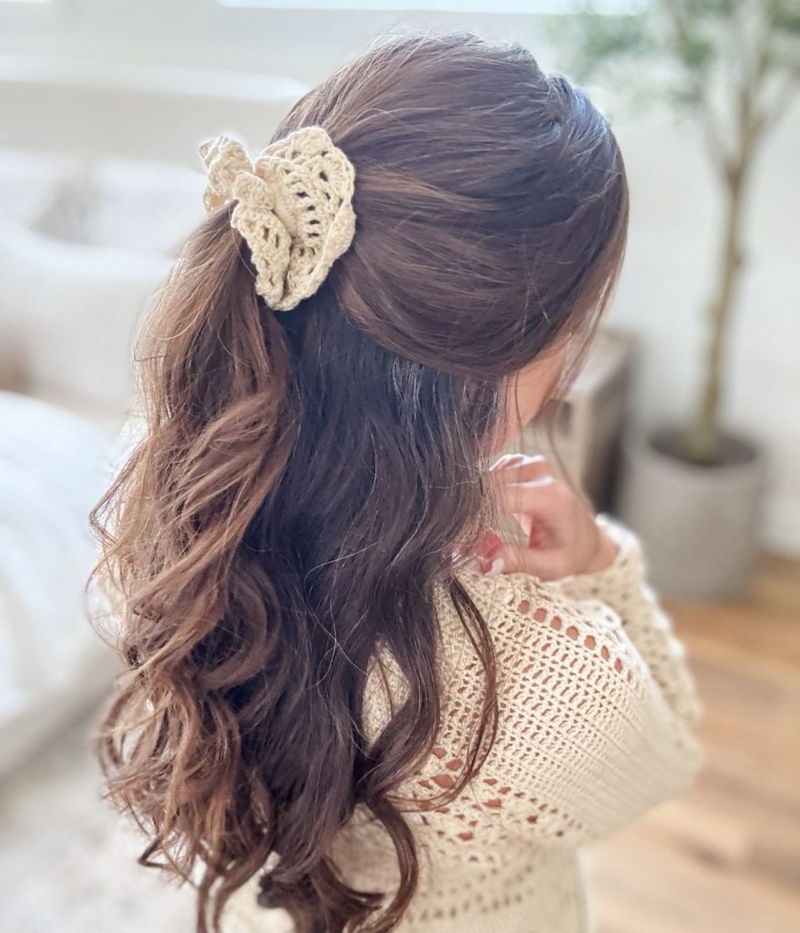 A woman with long, wavy brown hair styled half-up and secured with a crocheted butterfly hair clip, wearing a cream Caribbean Crochet Cardigan.
