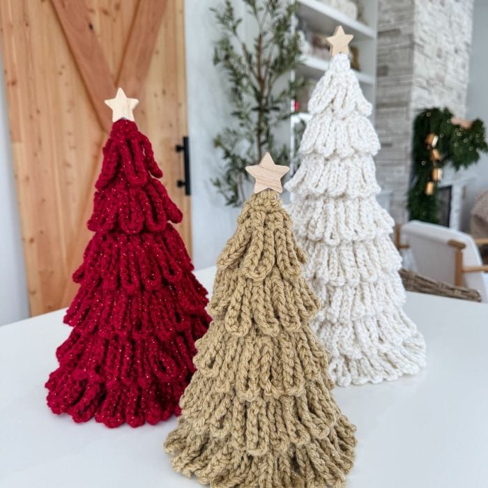 Three knitted Christmas trees in red, beige, and white with wooden star toppers are displayed on a white surface in a modern home setting—perfect inspiration for your next Loopy Crochet Trees project or Quick Crochet Pattern.