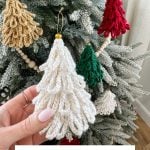 Hand holding a crocheted white Loopy Tree ornament in front of a Christmas tree decorated with colorful Loopy Tree crochet ornaments. Text reads, "Loopy Tree Ornaments. Free Crochet Pattern & Video.
