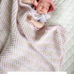 A baby sleeps on a quilted surface, wrapped in a pastel rainbow Alpine Stitch Blanket and wearing a pink crochet hat. Text reads: "Rainbow Peaks Blanket. Crochet Pattern & Video.