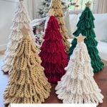 Six Loopy Crochet Trees in beige, red, and green with wooden star toppers are arranged on a table; a decorated tree glows in the background. Text reads: "Bulky & Quick Loopy Trees.