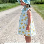 A young child wearing a blue crochet baby sunhat and lemon-print dress stands on a gravel path outdoors. Text reads: "Baby Sand Sunhat Pattern. Crochet Pattern & Video.