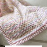 A multicolored crochet blanket with a textured alpine stitch pattern is draped over a light-colored couch. Text overlay reads: "Rainbow Peaks Blanket. Crochet Pattern & Video.