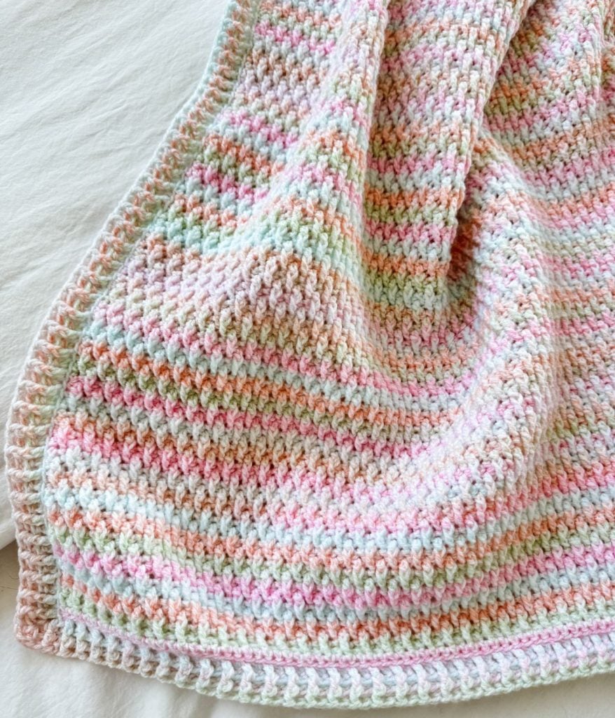 A pastel-colored Alpine Stitch Blanket with a textured pattern is draped over a light surface.