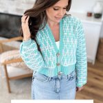 Woman wearing a light blue and white crocheted cardigan with buttons, standing indoors; text below reads "Seaglass Cardigan, Inset Mosaic Crochet Pattern & Video, inspired by the charm of the Old Town Sweater. Sizes XS-5X.