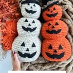 Two Crochet Jack-O-Lantern stacks, one white and one orange, each with three pumpkins and black witch hats, are displayed on a furry blanket beside yarn and autumn leaves.