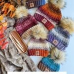 Five Chunky Suzette Stitch Beanies with faux fur pom-poms are arranged on a textured blanket next to crochet hooks and autumn leaves. Text reads: “Chunky Suzette Stitch Beanie Crochet Pattern & Video.”.