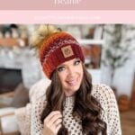 Woman wearing a chunky Suzette Stitch Beanie with a pom-pom, sitting indoors by a fireplace, smiling at the camera. Text above promotes a crochet pattern for the beanie.
