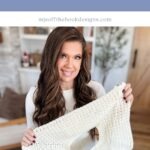 A woman holds up a partially finished white crocheted sweater, demonstrating the Suzette Raglan Sweater pattern.