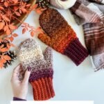 Two chunky, multicolored crochet mittens are displayed with a matching yarn ball, pine cones, and autumn leaves on a white surface. Text reads: "Chunky Suzette Stitch Fingerless Gloves and Mittens.