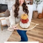 A woman in a crochet sweater holds a tray with three Harvest Pumpkins in autumn colors, sitting in a cozy living room. Text at the bottom reads "Chunky Harvest Pumpkins Free Crochet Pattern & Video.
