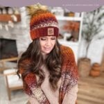 Woman wearing a crocheted hat and cozy pocket shawl in autumn colors stands indoors; text above reads "Chunky Suzette Stitch Pocket Shawl Crochet Pattern & Video.