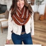 Woman wearing a chunky, multicolored Infinity Scarf stands indoors, smiling at the camera. Text below reads: "Chunky Suzette Stitch Infinity Scarf Crochet Pattern & Video.