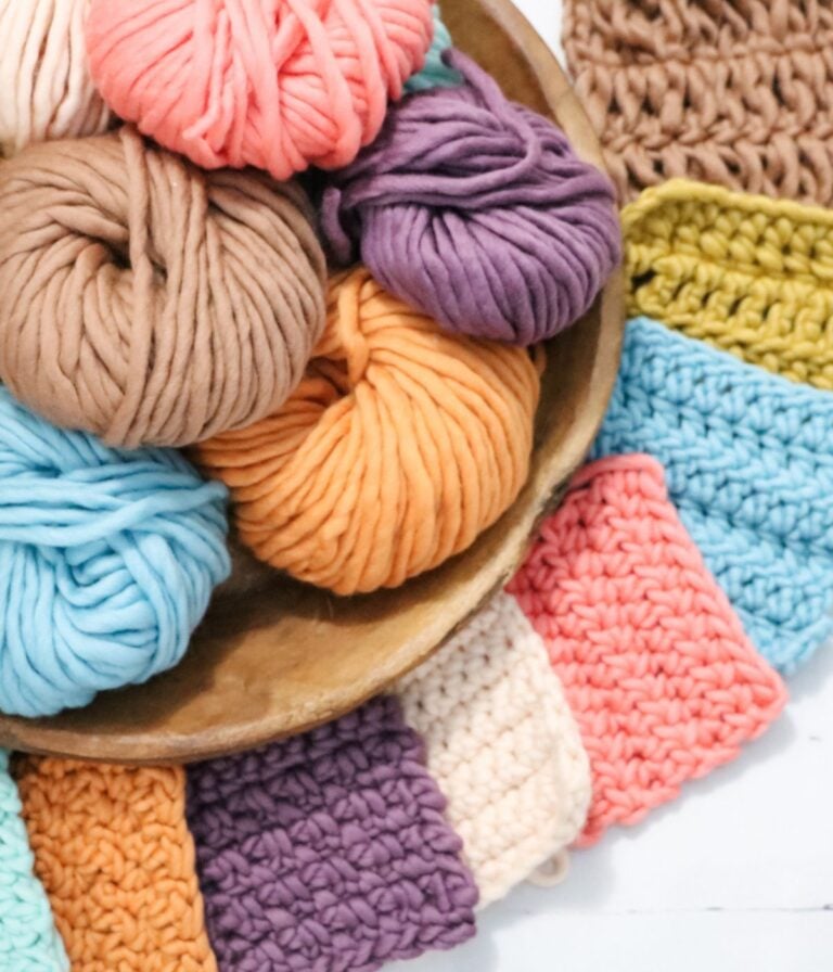 A wooden bowl filled with colorful skeins of yarn, surrounded by crocheted swatches in various pastel and bright colors.