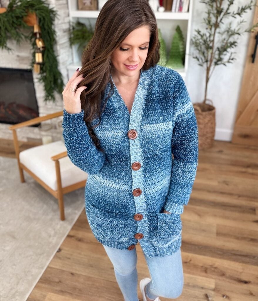 A woman with long brown hair wears an Everyday Cardigan in blue ombre and light jeans, standing in a living room with wood floors and plants.