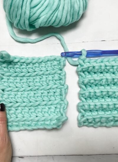 Two swatches of aqua chunky yarn crochet; one flat and one ribbed, with a large blue crochet hook and a ball of yarn in the background. A hand holds the flat swatch.
