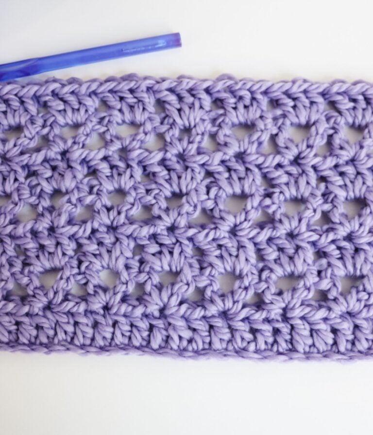 A rectangular swatch of lilac-colored crocheted fabric with an open, lacy pattern is shown beside a purple crochet hook on a white background.