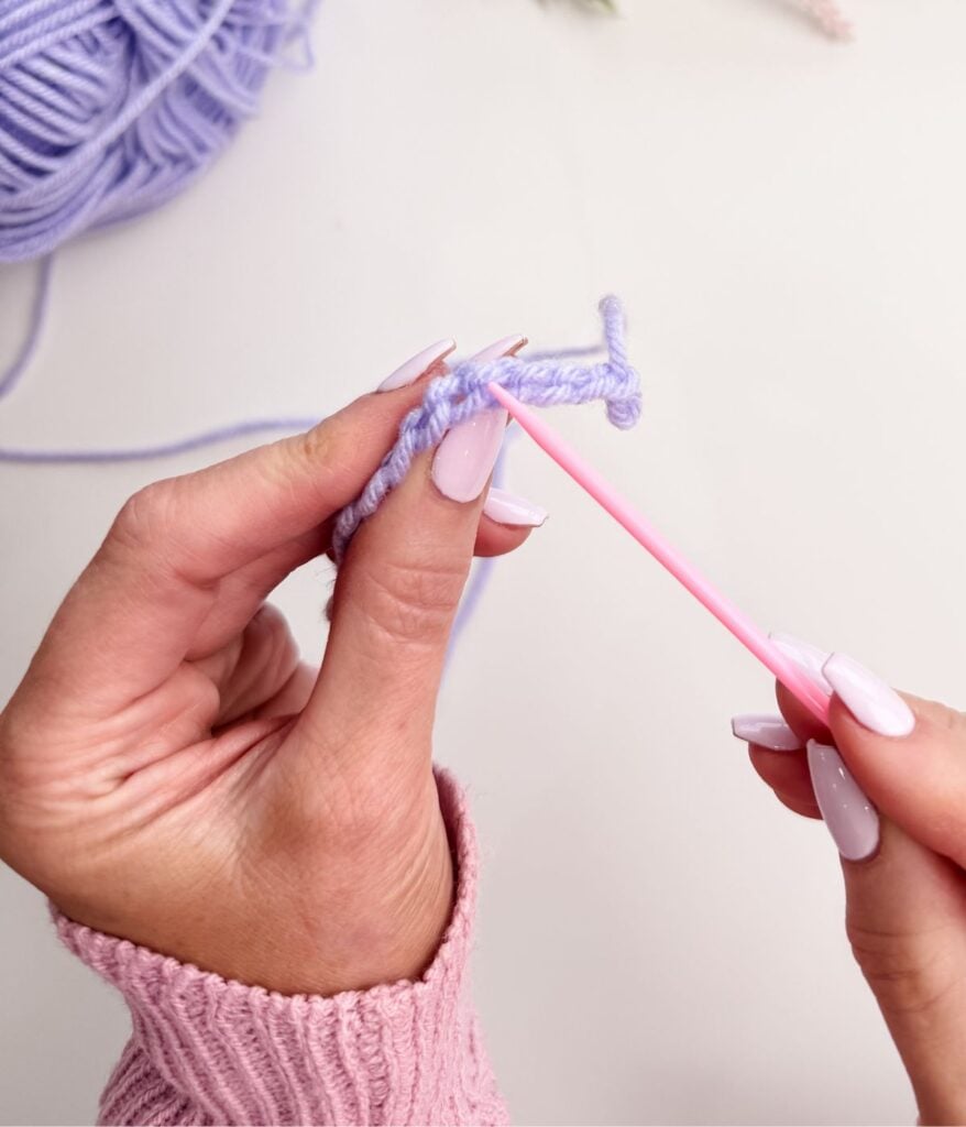 A person knitting with a needle starts by making a slip knot, followed by creating a neat row of chain stitches.