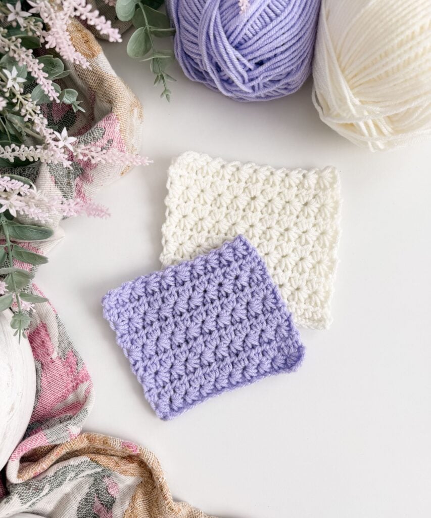 Two rectangular crochet swatches, one white and one lavender, are displayed on a white surface next to purple and white yarn balls and decorative flowers—perfect for anyone wanting to Learn Star Stitch or explore a Star Stitch Tutorial.