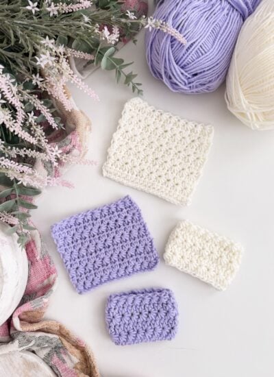 Four crocheted swatches in white and lavender yarn showcase the Crochet Star Stitch on a table beside yarn balls, flowers, and a scarf.