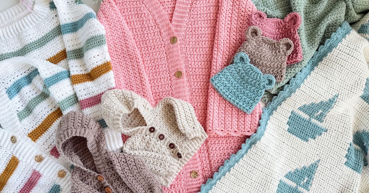 A collection of crocheted items including sweaters, hats with bear ears, mittens, and a blanket with blue patterns, displayed flat on a surface.
