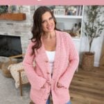 Woman stands indoors wearing a pink crocheted cardigan; fireplace, shelves, and plant in the background. Text promotes a star stitch reversible crochet pattern for cardigans.