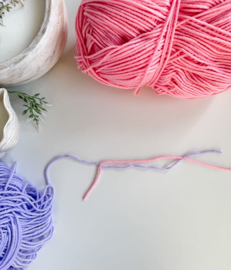 Pink and purple yarn balls with matching strands laid out on a white surface, near a plant in a white pot—a perfect setup for practicing how to join yarn using different crochet techniques.
