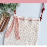 A crocheted shell stitch beach bag with a pink scarf tied to the handle, crochet hook, and yarn beside it. Text reads “Shell Stitch Bag Pattern” and “Easy Beach Bag Pattern.”.